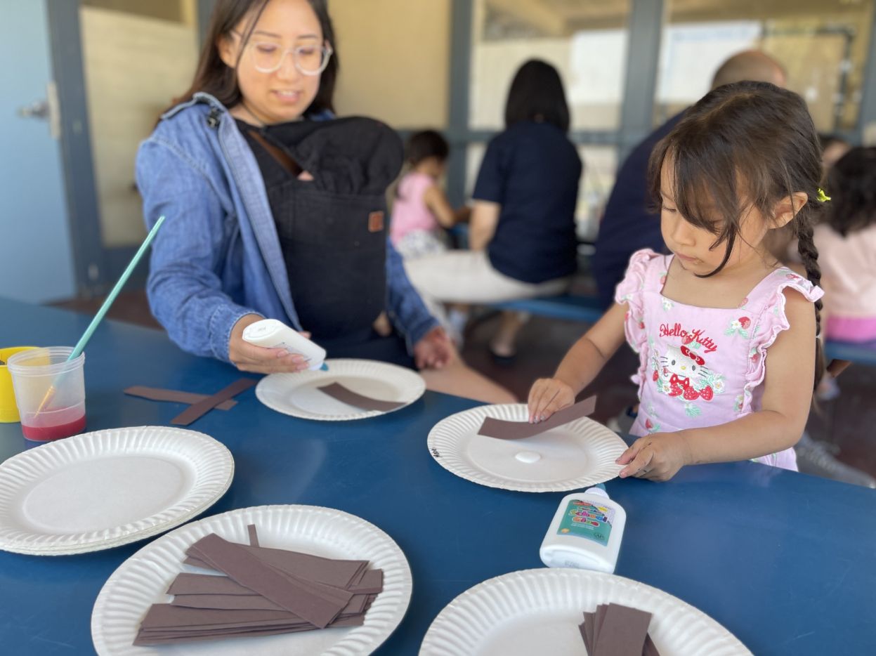 An adult helps a young child create a paper craft
