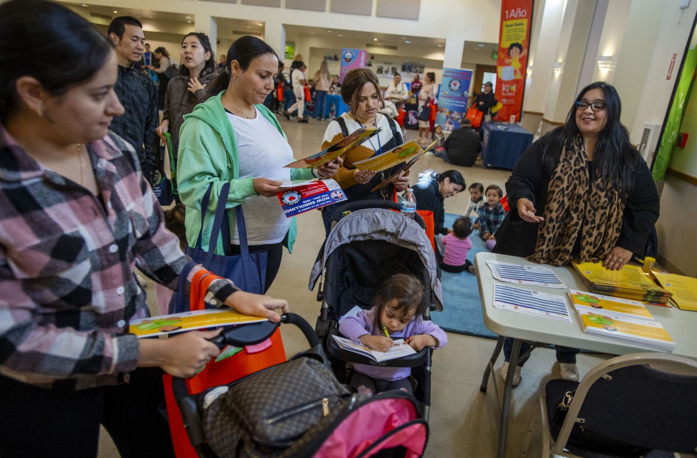 Families and volunteers gather around a table of books and learning resources